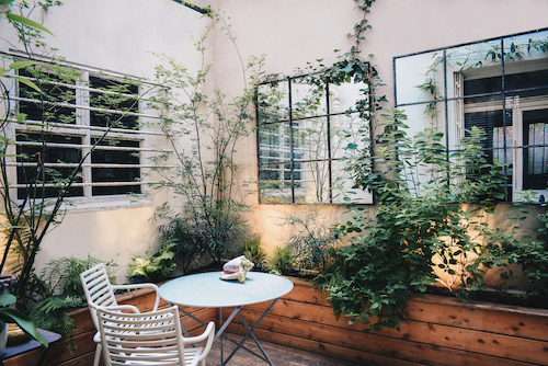 Photo d'un jardin terrasse imaginé par Atelier DLV, expert en maîtrise d'oeuvre jardins. On y voit une table ronde et des chaises, de nombreuses plantes et végétaux, des jeux de miroirs pour capter la lumière et agrandir l'espace